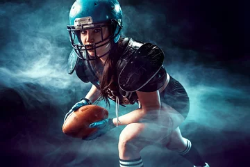 Tuinposter Sportive serious woman in helmet of rugby player holding ball in smoke. © zamuruev