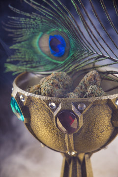 Close up detail of cannabis nugs on a calix with smoke and peacock feather