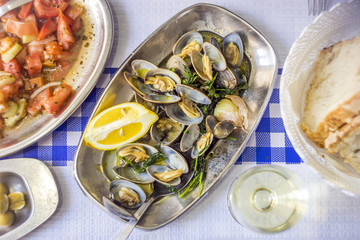 Clams served on silverware, tomato salad, bread, olives and white wine