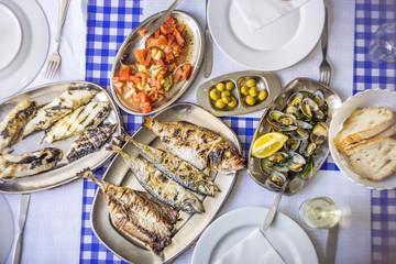 Barbecued sea bass, golden, horse mackerel accompanied with tomato salad, clams, bread and white wine
