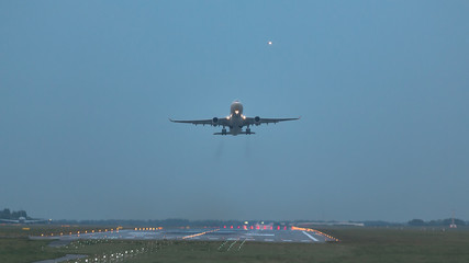 Wide-body modern civil airliner take off from runway in the evening, front view, silhouette plane in the sky on background/ Landing light leading to runway/ Vacation, aviation, travel, trip - concept