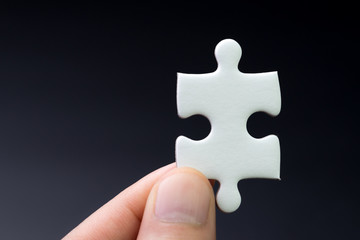 Obraz premium Business strategy missing piece, solution for success concept, hand holding a bright white paper jigsaw puzzle piece with dark black background