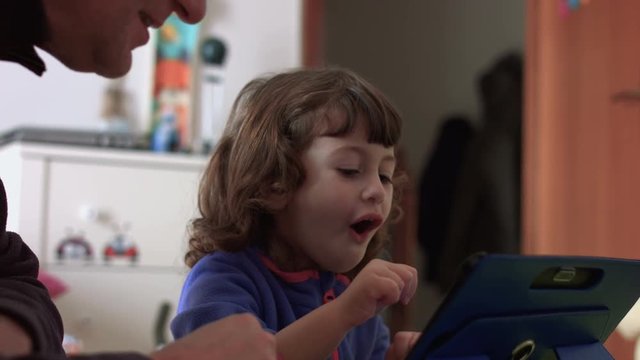 Candid nice daughter playing on a tablet with dad, joking and winning (close shot)