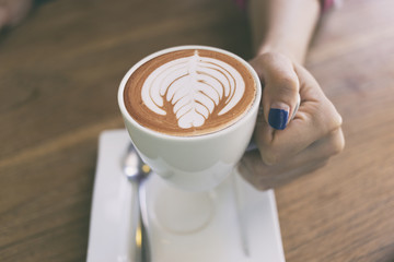 A hand of woman holding a cup of coffee art heart shape.