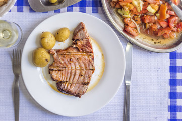 Tuna steak accompanied with potatoes, olives, tomato salad and wine