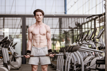 Fototapeta na wymiar A shirtless young muscular man working out in gym doing exercises with equipment in fitness center.