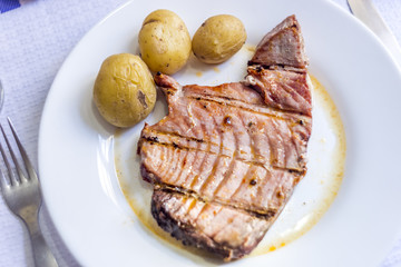 Tuna steak with potatoes served on white plate