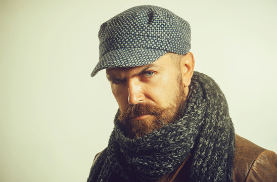 Serious man with beard, brutal caucasian hipster wearing warm scarf wrapped around his neck, cap on head and jacket. Advertising autumn-winter fashion. Copy space.