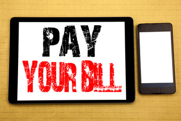 Hand writing text caption inspiration showing Pay Your Bill. Business concept for Payment for Goverment Written on tablet laptop, wooden background with sticky note, coffee and pen