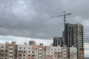 Fototapeta na wymiar a crane standing over a tall block-of-flats with epic huge clouds on the background