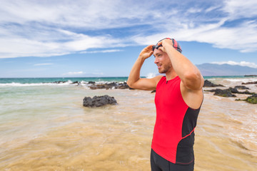 Man triathlete swimmer putting on swim goggles - Triathlon sport athlete going swimming getting ready an ocean swim. Fit man in professional triathlon suit training for ironman.