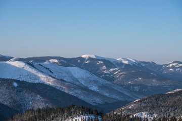 Winter landscape in the mountains with blue sky and snow-capped peaks and forest