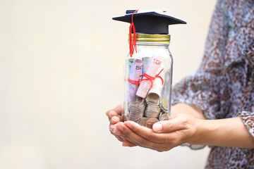 Woman hand holding coins money and banknote in glass bottle with graduates hat on white background, Mother to save money for education children