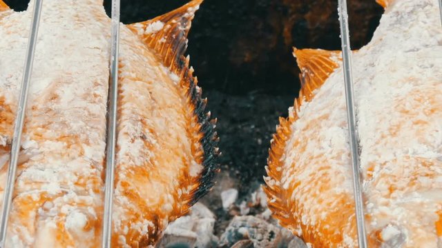 National Thai dish, fried fish on spit in salt and with greens close up view. Exotic food of Thailand and Asia