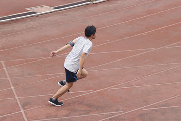 Young Asian sprinter leaving starting on racetrack at athletics stadium.