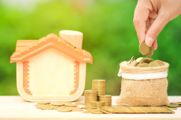 Hand of the female putting money coin into the bag on natural green background, Saving money for new home and prepare in the future concept.