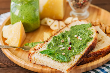 Bruschetta with basil walnut pesto sauce on a wooden plate. Wooden backdrop. Close up.