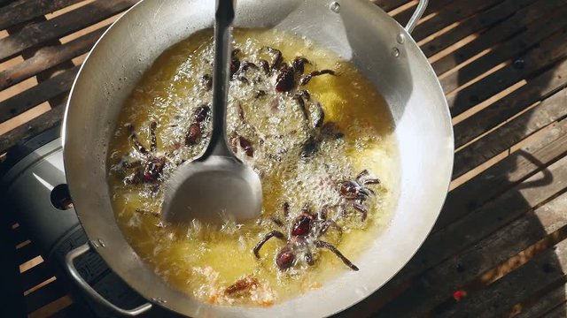 Woman turning over deep frying tarantulas inside a wok using a metal spatula (close-up upper view)