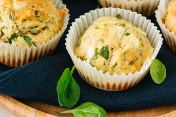 Savory muffins with feta cheese and spinach on a wooden plate on a wire rack.White stone backdrop.