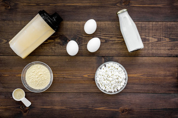 Fototapeta na wymiar Protein diet for the athlete Scoop of protein near shaker, milk, eggs, cottage cheese on dark wooden background top view copy space