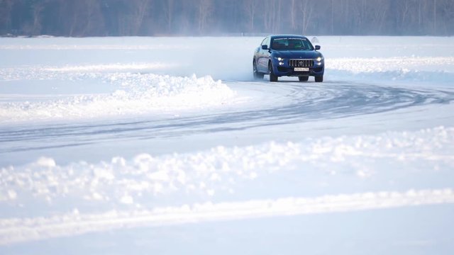 Winter driving. Blue car drives by icy track on snow covered lake at winter. Sport car racing on snow race track in winter. Driving a race car on a snowy road