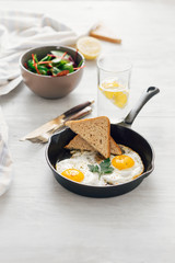 Fried egg in frying pan on white wooden table with salad and lemon water. Breakfast table