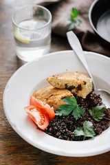 Close up plate with black quinoa and oatmeal cutlets with prunes on wooden table with glass water with lemon. Vegetarian dinner table