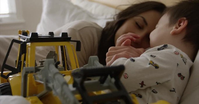 Toddler boy and mother lay down for afternoon nap with toy backhoe - cute family time