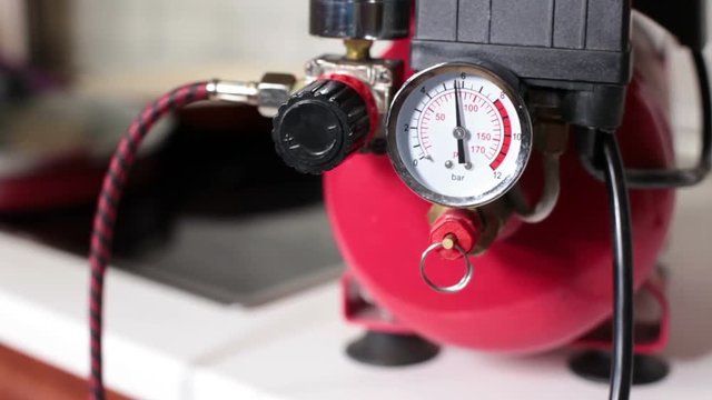 Gauge hand indicated pressure boosting with working small portable piston-type air compressor standing on the table