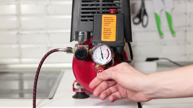 Man's hand relieves pressure in small portable piston-type air compressor standing on the table