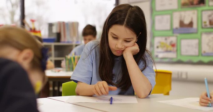 4K Portrait unhappy or bored little girl working at a communal table in school classroom. Slow motion