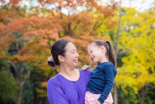 Asian woman holding her daughter and smiling together in autumn park