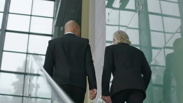 two corporate executives talking discussing business while ascending stairs in company.  