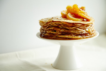 Crepes cake with orange jam and honey on white cake stand. Pancake breakfast concept