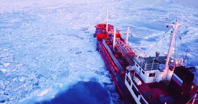 Close aerial view of the ship slowly moving through ice floes. Flying above the Eastern Bosphorus strait. Vladivostok, Russia. Evening