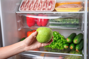 Young woman taking apple from refrigerator, closeup