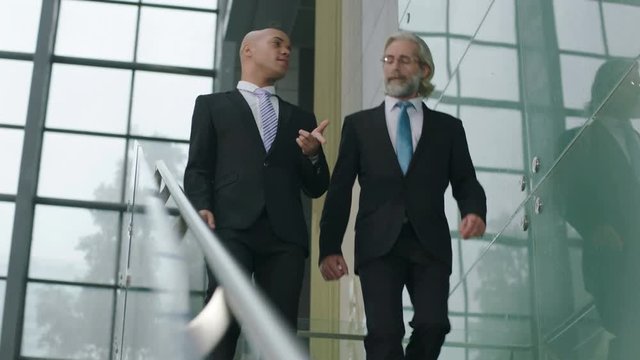 two corporate executives talking discussing business while descending stairs in company.