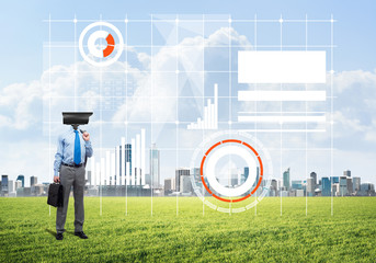 Camera headed man standing on green grass against modern cityscape