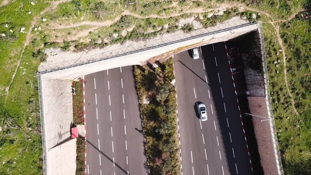 Highway traffic entering and exiting a Toll collection stop leading to a double tunnel surrounded by green landscape - Aerial footage
