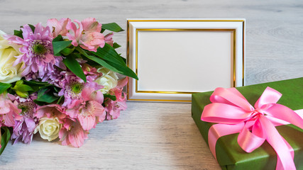 Colorful bouquet of roses, chrysanthemum and alstroemeria flowers with gift box and empty photoframe on wooden background