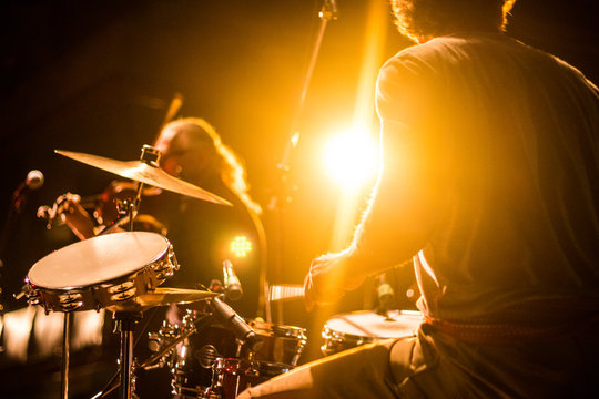 Drummer on stage playing with a band with gold yellow light shining in background 