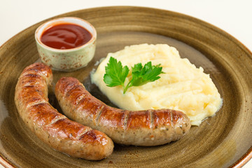 Mashed potatoes and two fried sausages with ketchup sauce in a large plate.
