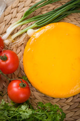 Homemade organic cheese head in yellow vacuum package with Tomatoes, Basil, onions herbs on wooden board on the table. Healthy food, snack and eating.