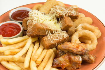 French fries, onion rings, chicken wings, rusks, a snack to beer on a large plate with two sauces on a brown background.