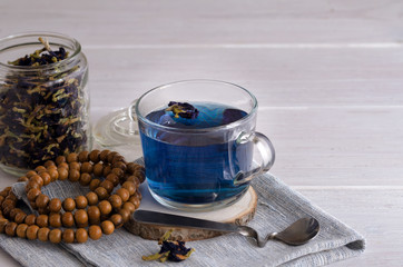 Close up of Butterfly pea flower tea cup and mala beads,  dried flower of Clitoria Clitoria ternatea plant on the back. Asian exotic blue tea background with copy space