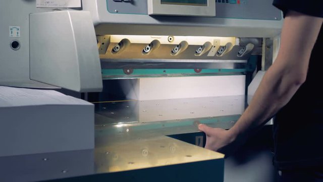Printing house worker operating cutting machine. Worker cutting a stack of paper in a typography.