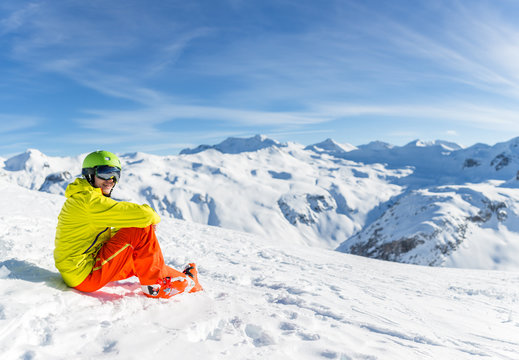 Image of sportive man wearing helmet wearing yellow jacket sitting on snowy slope