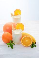 Smoothies with bananas and oranges, a sprig of mint on a white background. Space for text or design.