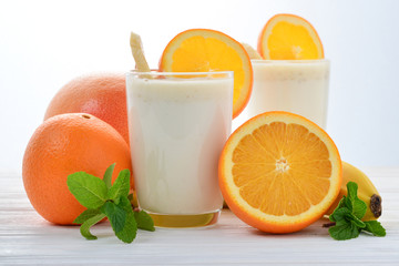 Smoothies with bananas and oranges, a sprig of mint on a white background. Space for text or design.