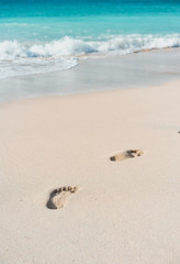 Fototapeta na wymiar Azure ocean waves rolling on the beach with foot prints